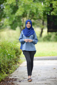 Full length portrait of young woman standing on footpath