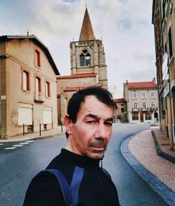 Portrait of young man standing against buildings in city