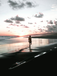 Silhouette man standing on beach against sky during sunset