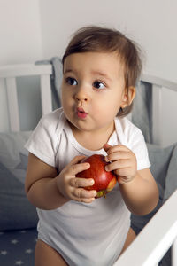 One year old baby boy sitting in bed with a red apple