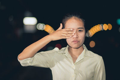 Portrait of woman covering eye against defocused light at night