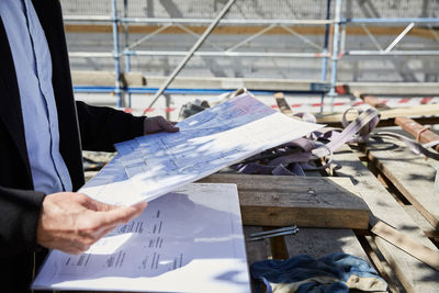 Midsection of architect with blueprint on table at construction site