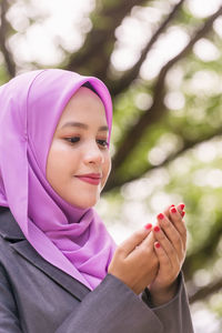 Smiling young woman praying while sitting in park