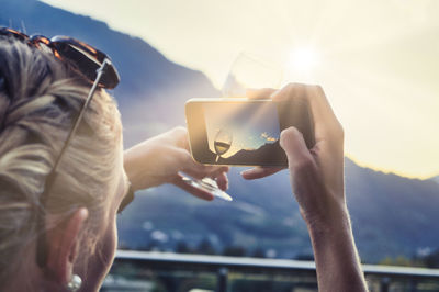 Midsection of man using mobile phone against sky during sunset