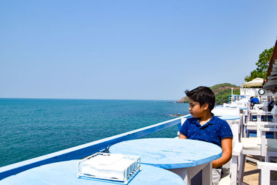 Boy sitting on railing against sea