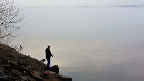 Man standing on rock by lake against sky