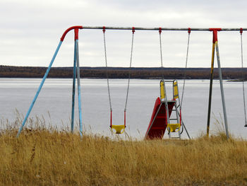 Empty swing hanging on beach against sky