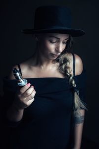 Close-up of young woman wearing hat against black background