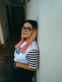 Portrait of smiling young woman standing against wall