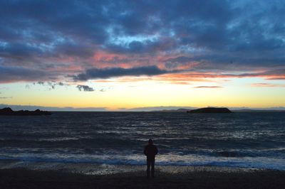 Silhouette man standing on beach against sky during sunset