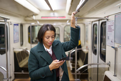 Businesswoman in subway wagon using smartphone to send business email or text message to family