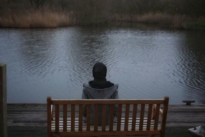 Rear view of man sitting on pier over lake