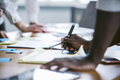 Cropped hands of businessman writing on sticky notes with colleague in board room