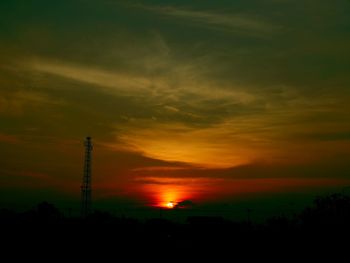 Silhouette electricity pylon against dramatic sky during sunset