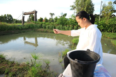 Young woman feeding fish at farm
