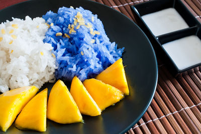 High angle view of white and blue rice with mango served in plate on place mat