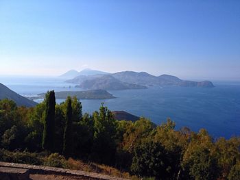 Scenic view of sea and mountains with trees against clear blue sky