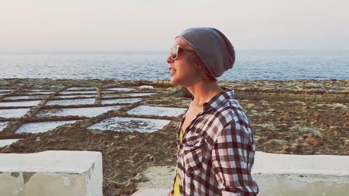 Young woman standing at beach against sky