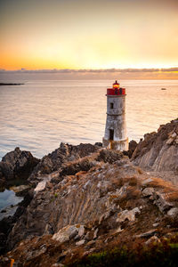 Lighthouse by sea against sky during sunset