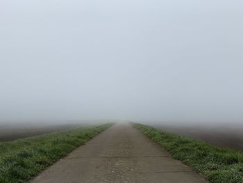 Empty road amidst field against sky