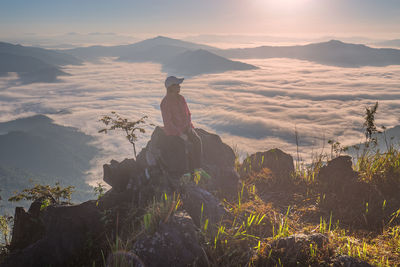 Man sitting on rock looking at mountains against sky