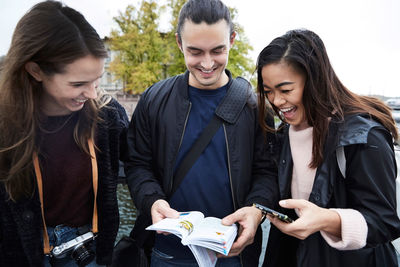 Happy friends looking at map while standing in city