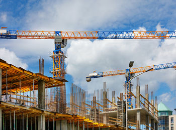 Tower cranes work at the construction site of a multi-storey residential building against a sky.