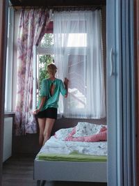 Rear view of woman standing by window at home