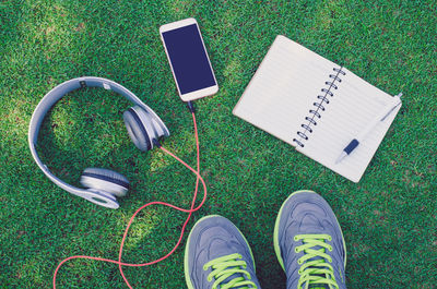 High angle view of sports shoe with headphones and diary on field