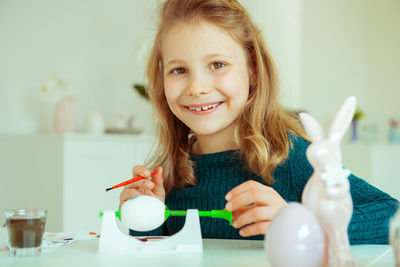 Portrait of cute girl painting easter egg while sitting at home