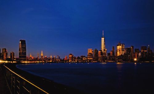 Illuminated cityscape by sea against sky at night