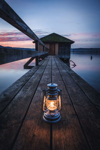 Illuminated lamp on pier by sea against sky at sunset