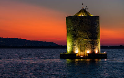 Built structure by sea against sky during sunset