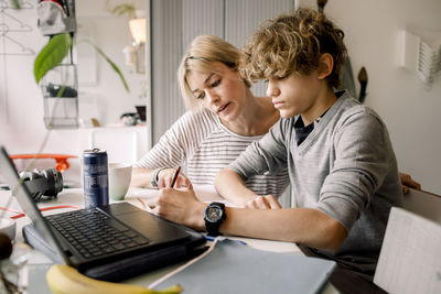 Mother guiding son doing homework while sitting at table