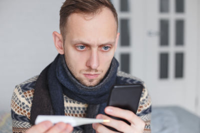 Man using mobile phone while holding thermometer