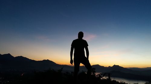 Rear view of silhouette man standing on mountain against sky