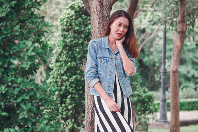 Portrait of young woman standing against tree trunk