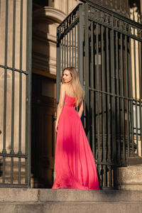 Low angle rear view of beautiful woman in pink evening gown standing at doorway