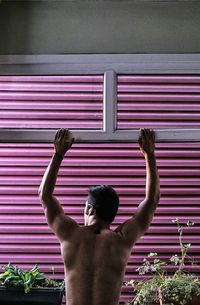 Rear view of shirtless man standing against wall