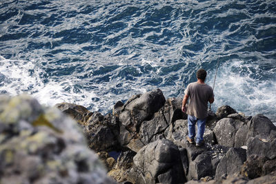 Rear view of man standing on rock at sea