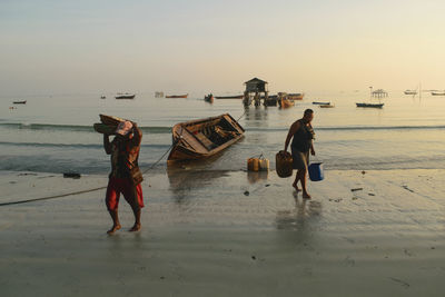 Fishermen working at beach against sky during sunset