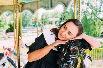 Beautiful brunette girl in a black dress poses on a bright carousel with horses