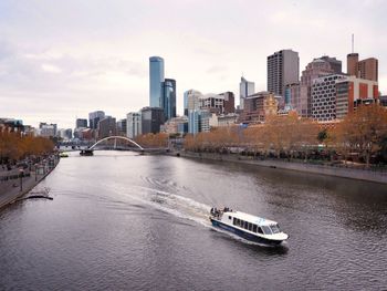 Nautical vessel on river by buildings in city against sky