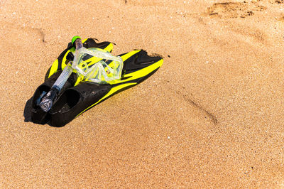 Snorkeling equipment on the sand with ocean waves splashing the water. black fins, black mask