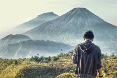 Rear view of man standing against mountain on field