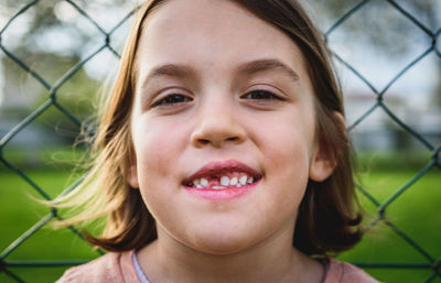 Close-up portrait of smiling girl against fence