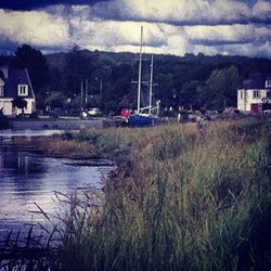 View of built structure by river against cloudy sky