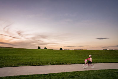 Happy young girl biking through a park with mowed grass