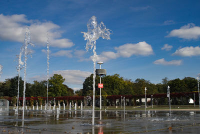 Fountain on field by lake against sky