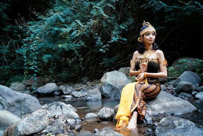 Young woman sitting on rock in forest